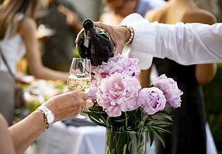 Hand schenkt Sekt in ein Glas ein, umgeben von rosa Pfingstrosen bei einer festlichen Veranstaltung