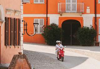 Personne circulant en Vespa rouge sur une place pavée historique devant un palazzo orange au Piémont